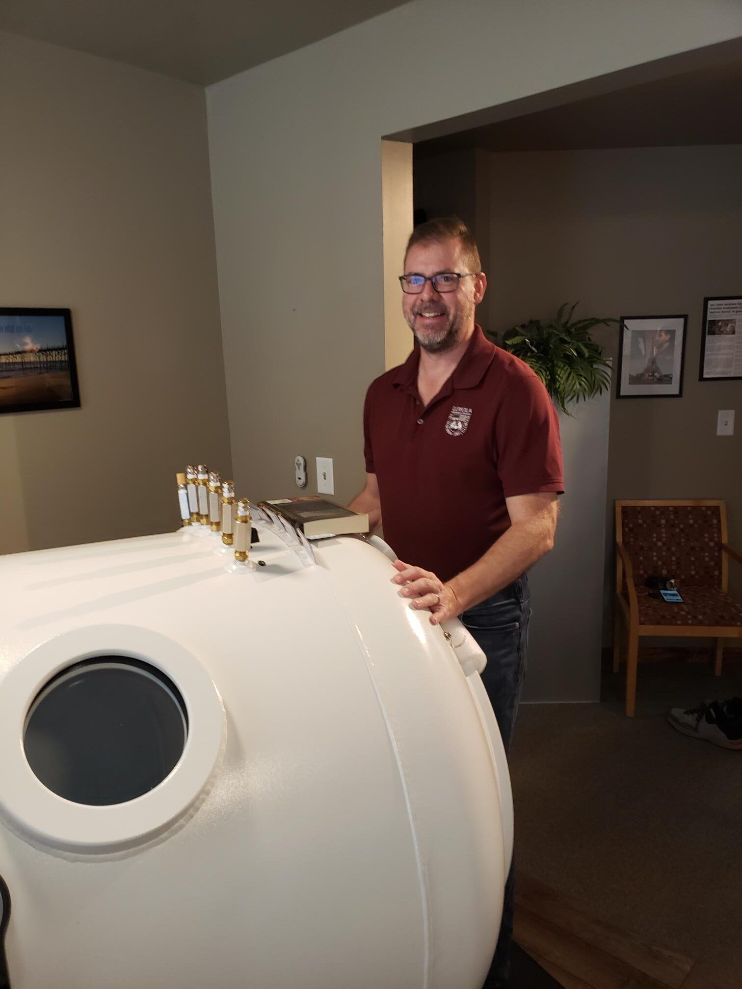 A man in a maroon shirt is standing next to a white cylinder in a room.