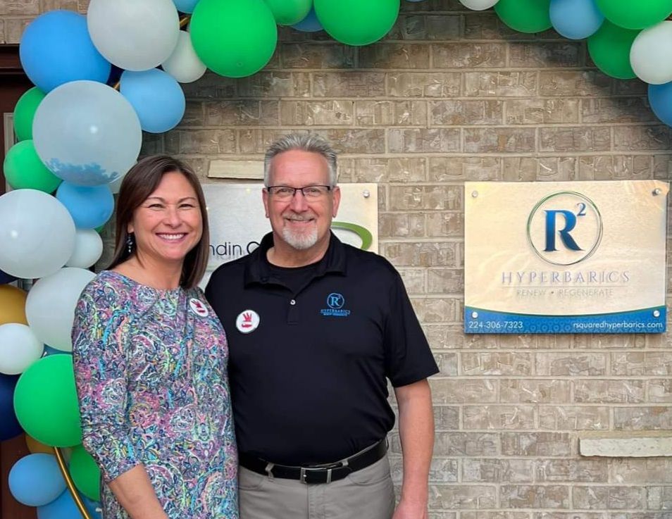 A man and a woman are standing in front of a brick wall with balloons.