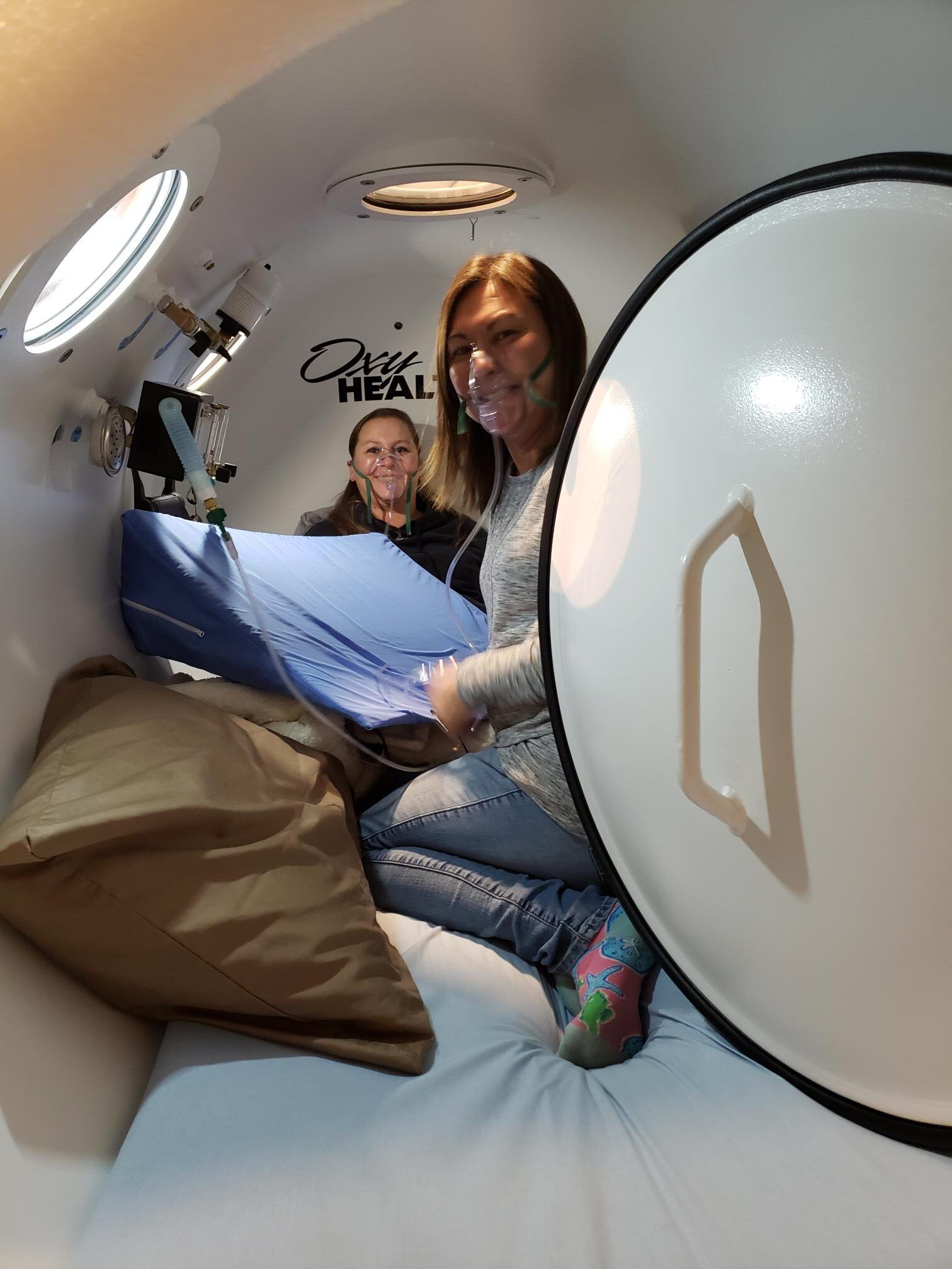 Two women are sitting on a bed in an oxygen chamber.