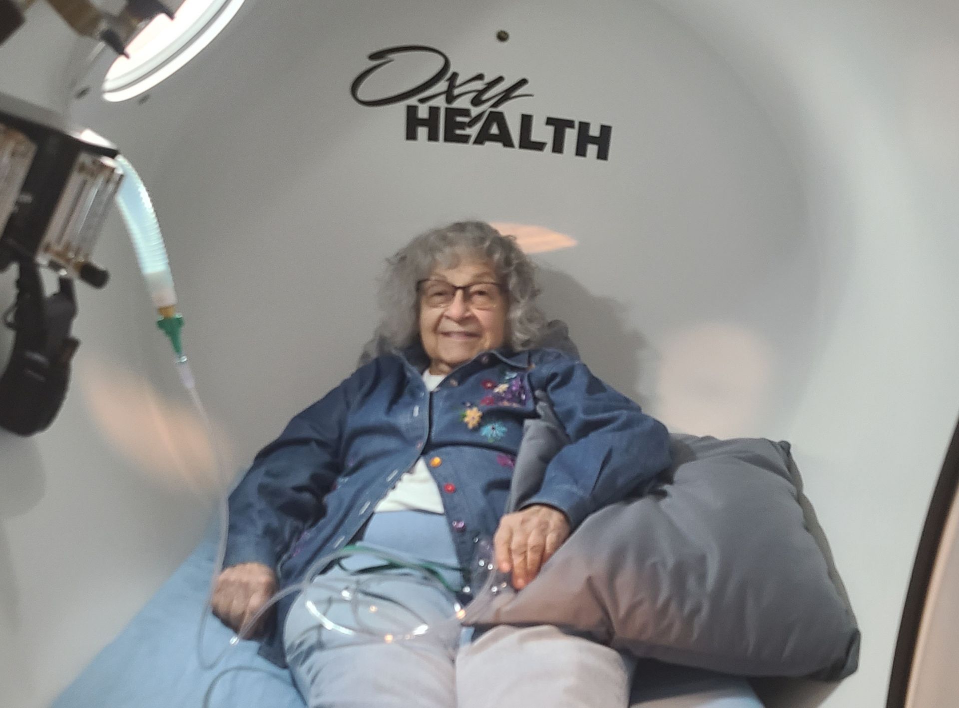 An elderly woman is sitting in an oxygen chamber