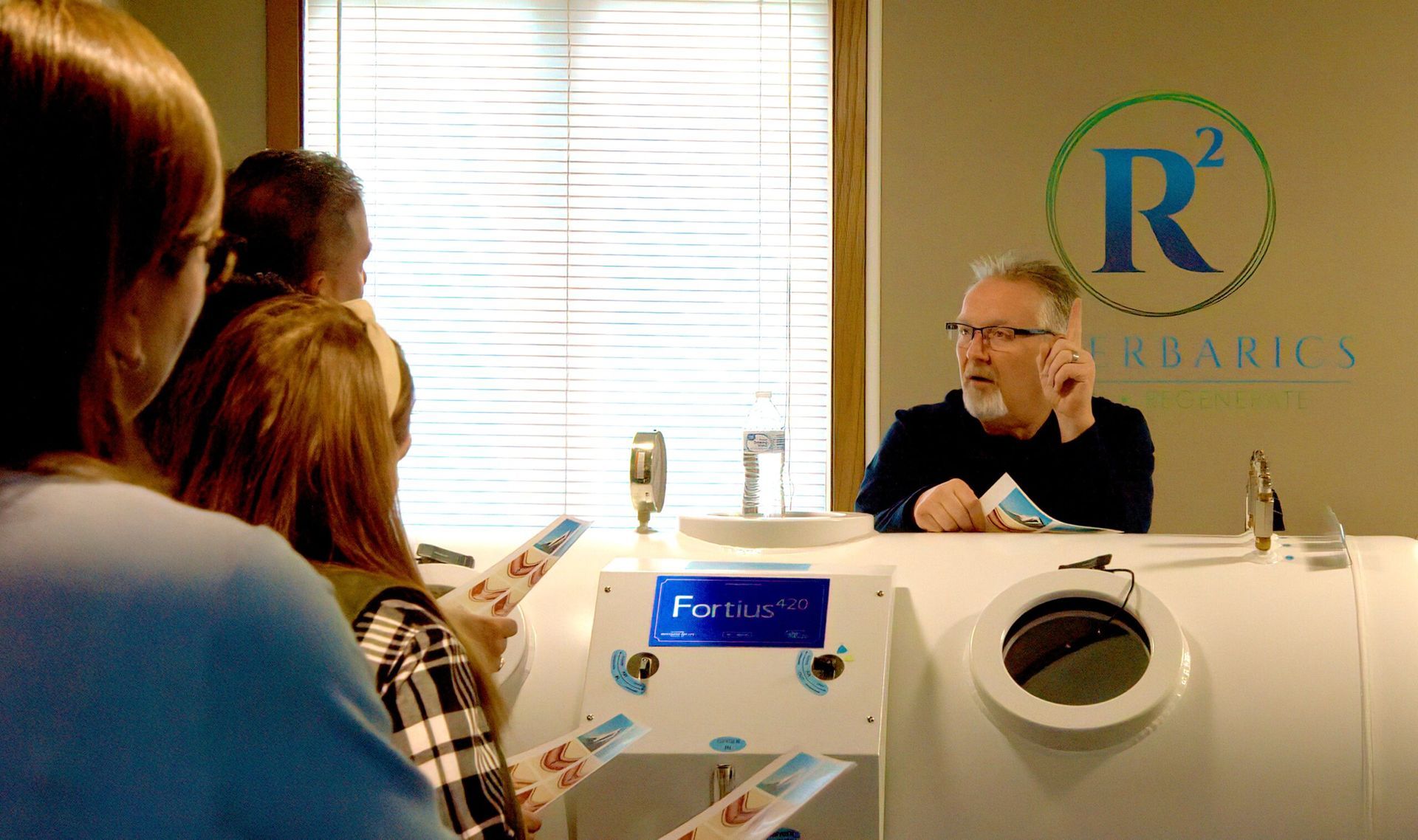 A man is talking to a group of people in front of a sign that says r2