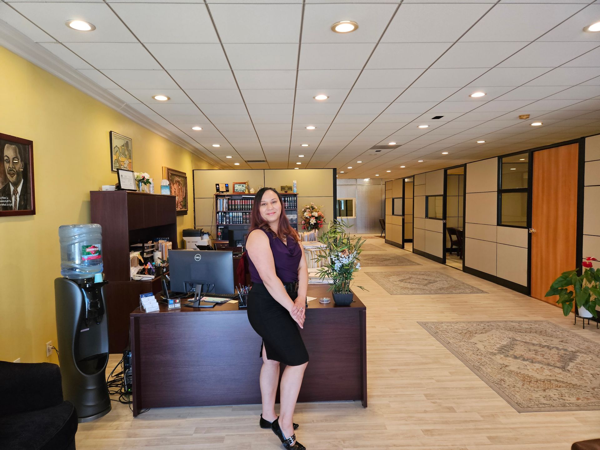 Woman standing at an office reception desk in a bright hallway lobby.