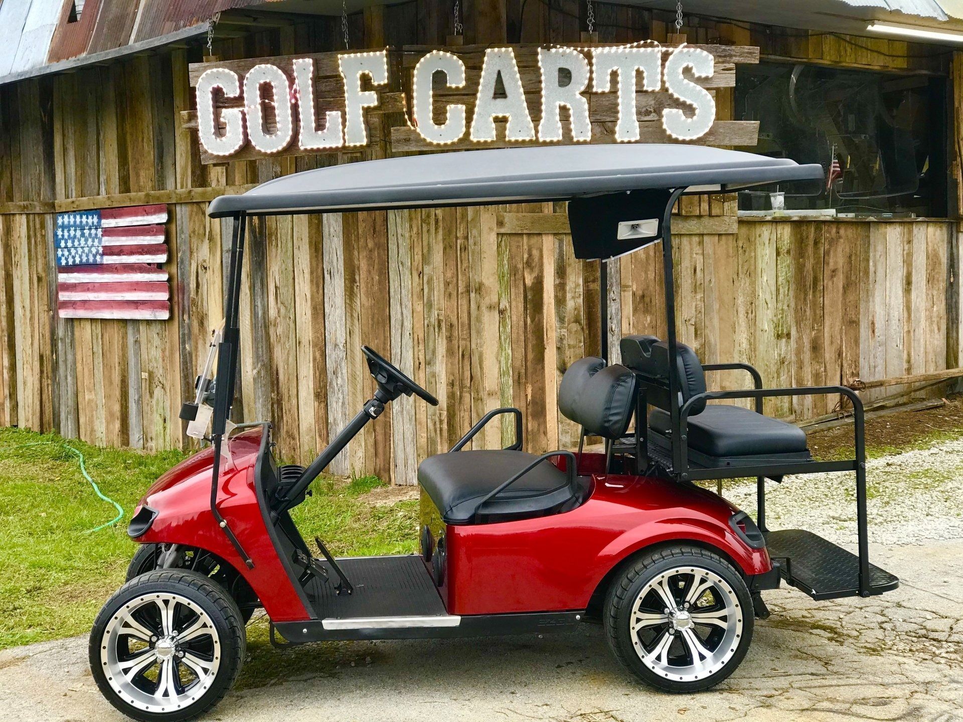 A red golf cart is parked in front of a wooden building.