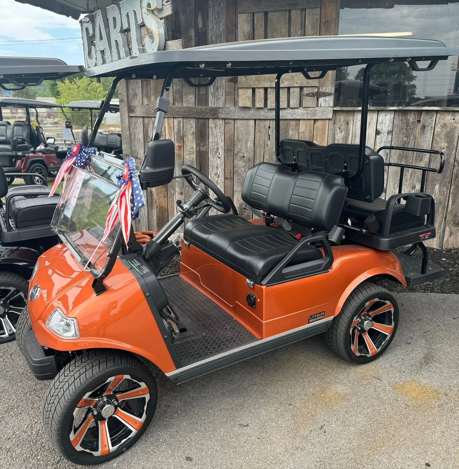 An orange golf cart is parked in front of a wooden building.