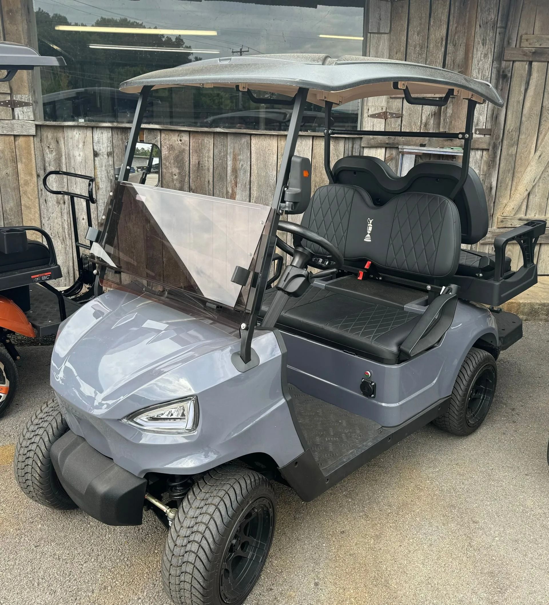 A gray golf cart is parked in front of a wooden building.