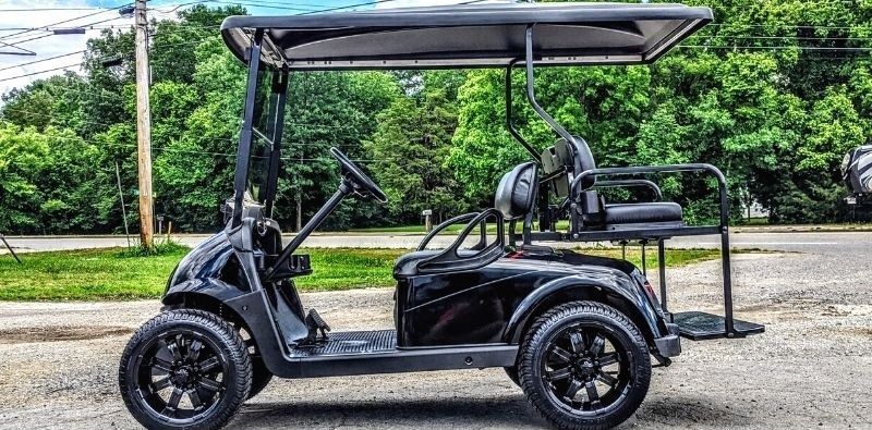 A black golf cart is parked on the side of the road.