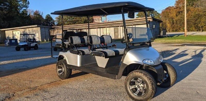 A silver golf cart is parked in a gravel lot.