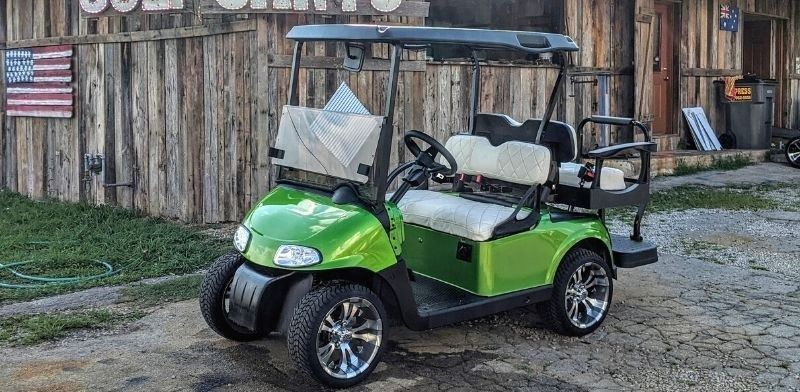 A green golf cart is parked in front of a wooden building.