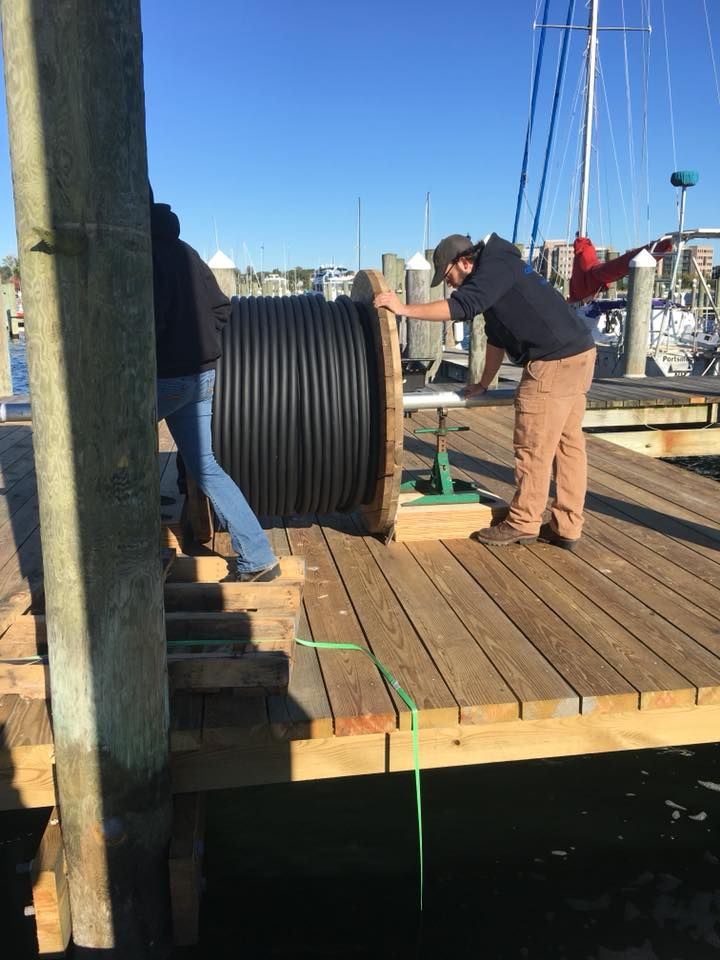 A man is holding a large spool of cable on a dock
