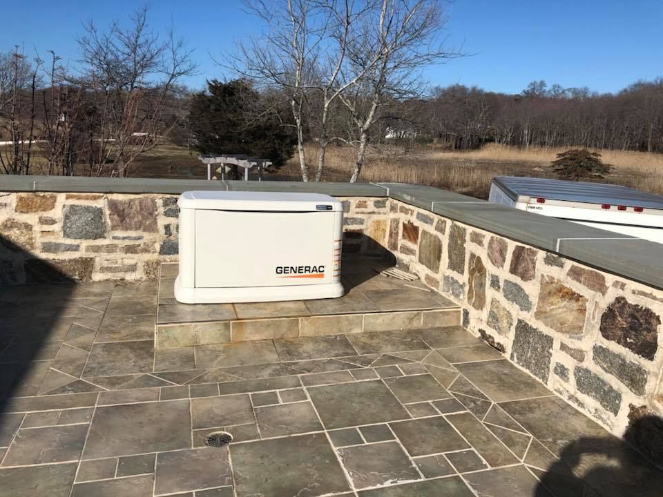 A generator is sitting on top of a tiled patio next to a stone wall.