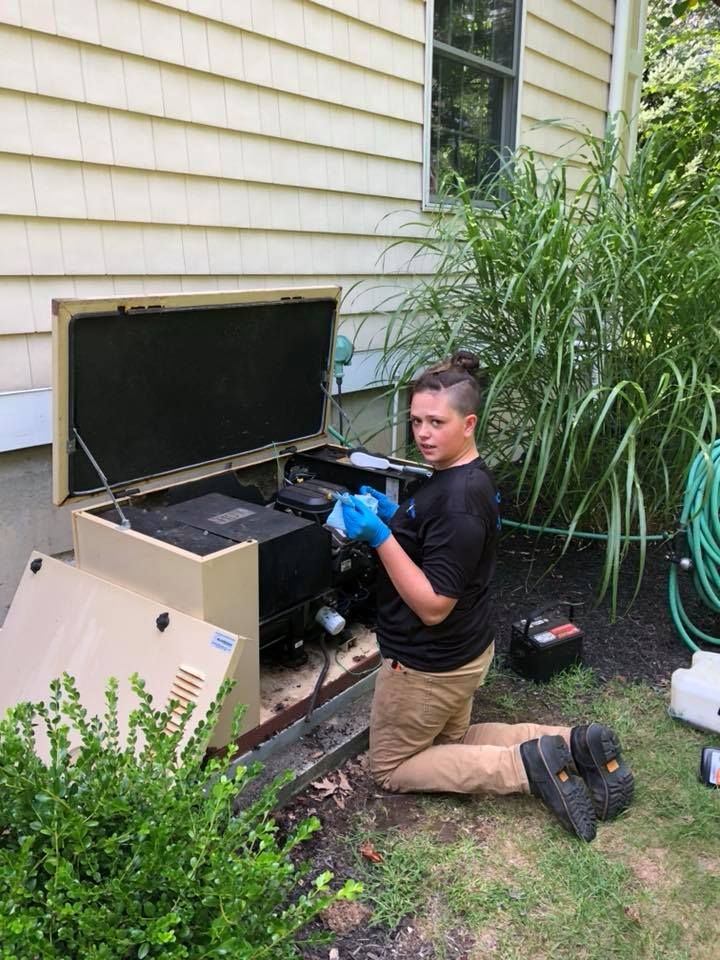 A man is kneeling down in front of a house while working on a generator.