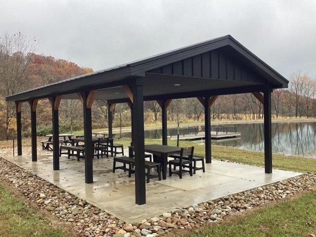 Open-sided pavilion with picnic tables beside a calm lake on an overcast day