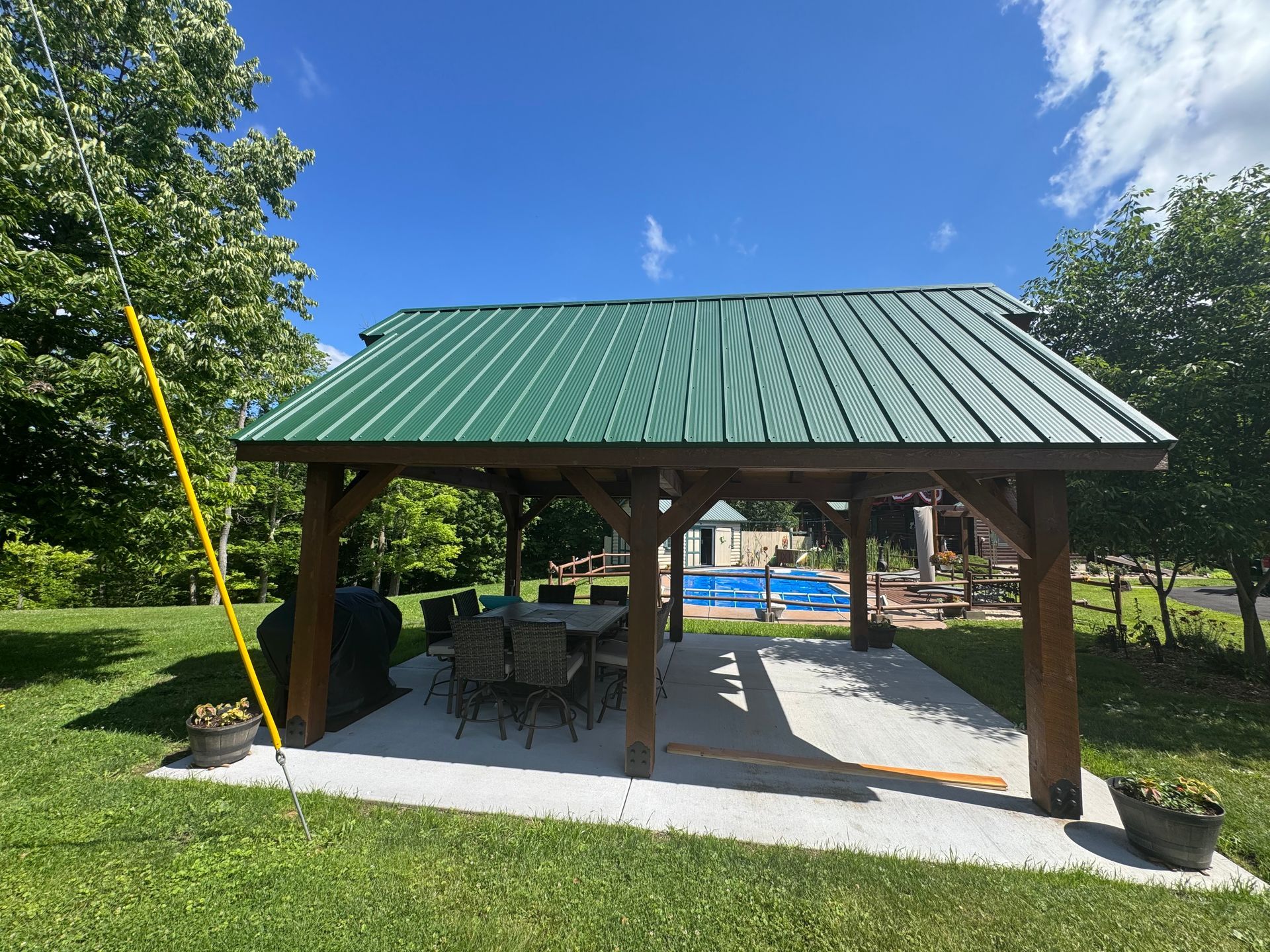 Open-air picnic pavilion with green roof, picnic tables, and poolside view in a sunny park