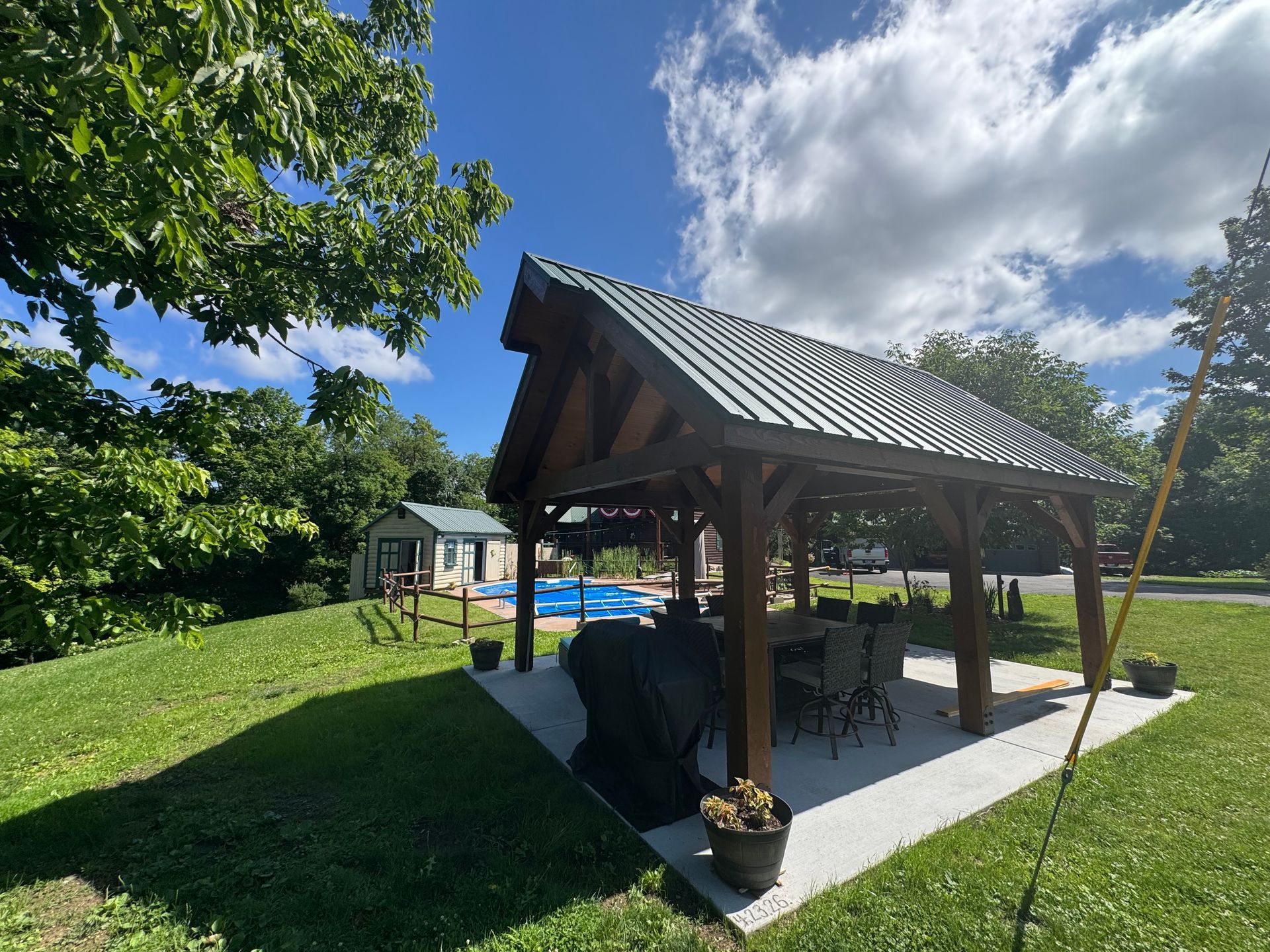 Open-air pavilion with wooden roof in a grassy backyard under a blue sky