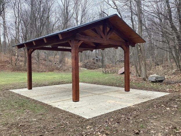 Wooden pavilion with a metal roof on a concrete pad in a wooded park