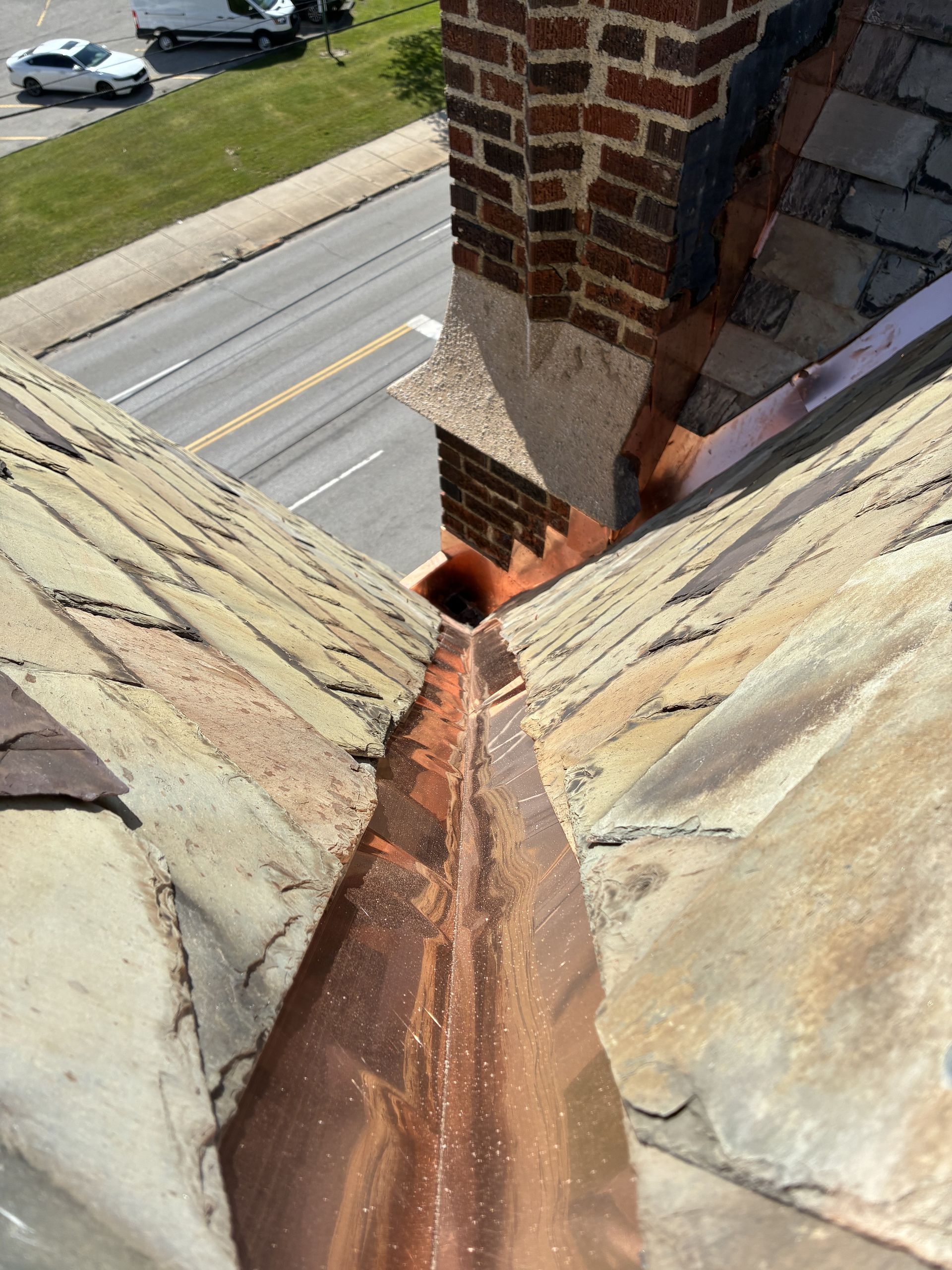 Close-up of a roof valley with rusted flashing and brick chimney beside asphalt shingles.