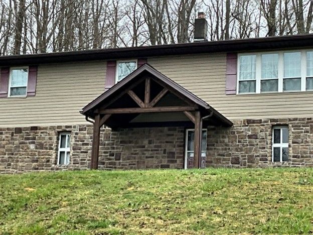 Stone house with a small wooden porch under a gable, set on a grassy slope with bare trees behind.