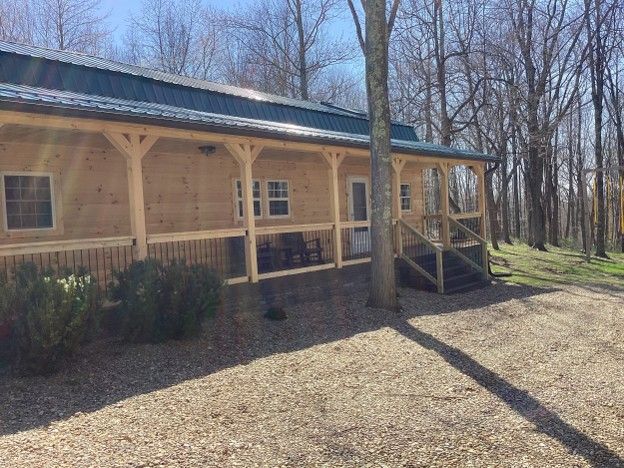 Wooden cabin porch with steps in a wooded yard on a sunny day