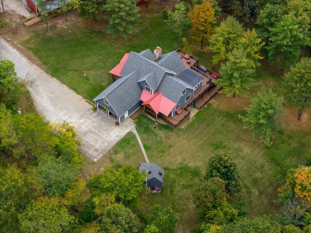 Aerial view of a house with a gray roof and red porch, surrounded by trees and lawn.