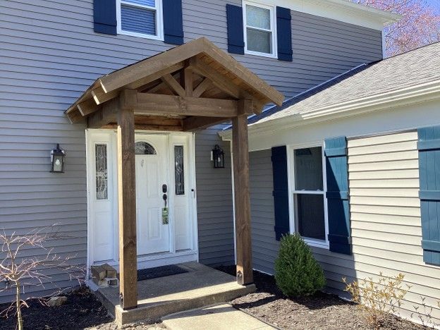 Covered front porch with wooden posts and a peaked roof over a white double front door on a house.