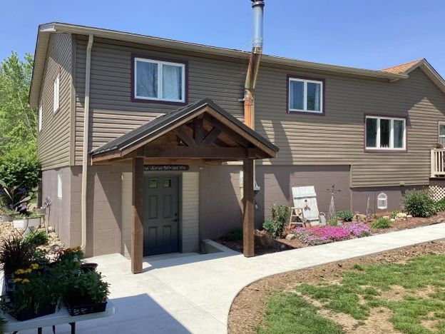 Two-story beige house with a covered front entrance, walkway, and small lawn on a sunny day