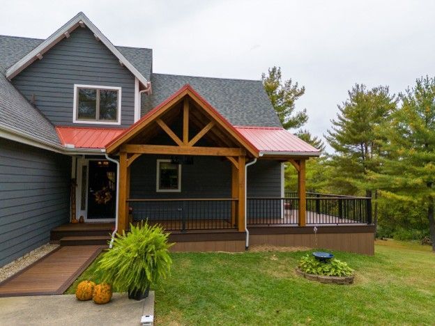 Gray house with wood porch and gabled entry, overlooking a green lawn and trees