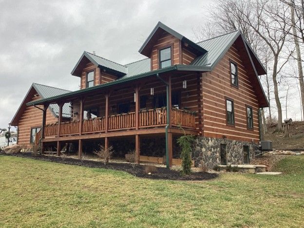 Log cabin-style house with a covered porch on a grassy hillside under overcast skies