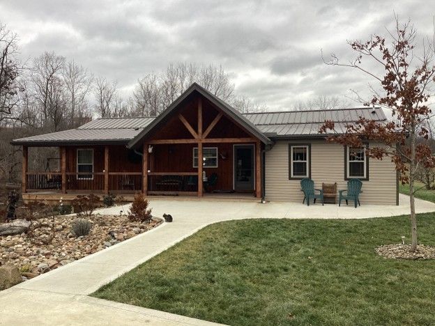 Single-story rustic house with a covered porch, walkway, and small lawn under a cloudy sky