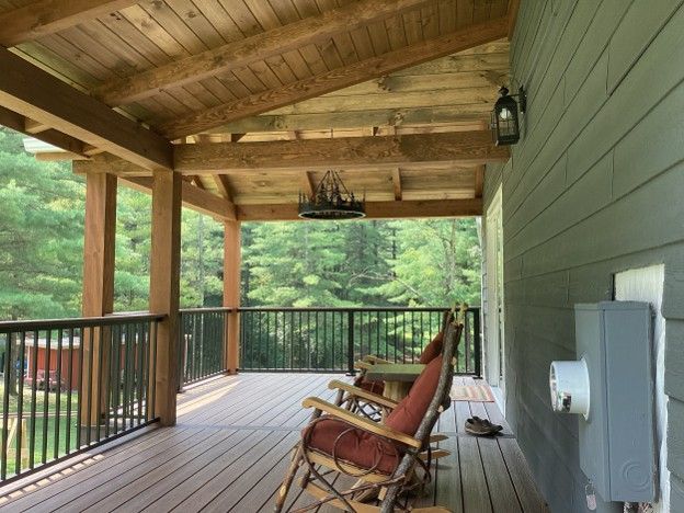 Covered wooden porch with rocking chairs, black railing, and forest view.