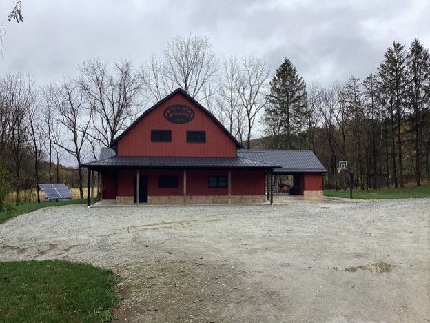 Red barn-style building with a dark roof in a gravel lot, surrounded by bare trees under an overcast sky
