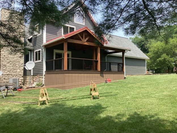House with covered porch, lawn, and trees in a suburban yard