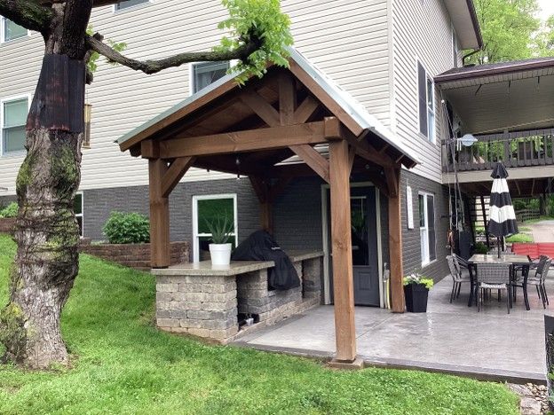 Backyard patio with a wooden covered grill station, potted plant, table, chairs, and a tree nearby