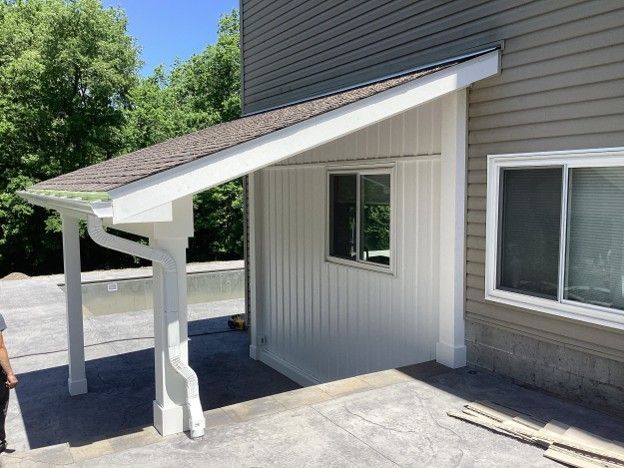 Covered wheelchair ramp and awning beside a building entrance with white railings and beige siding