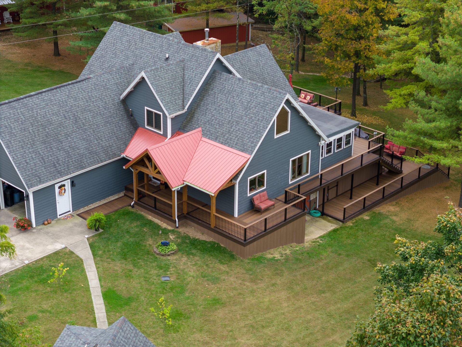 Aerial view of a gray house with red roof over a large grassy yard and wooden deck.