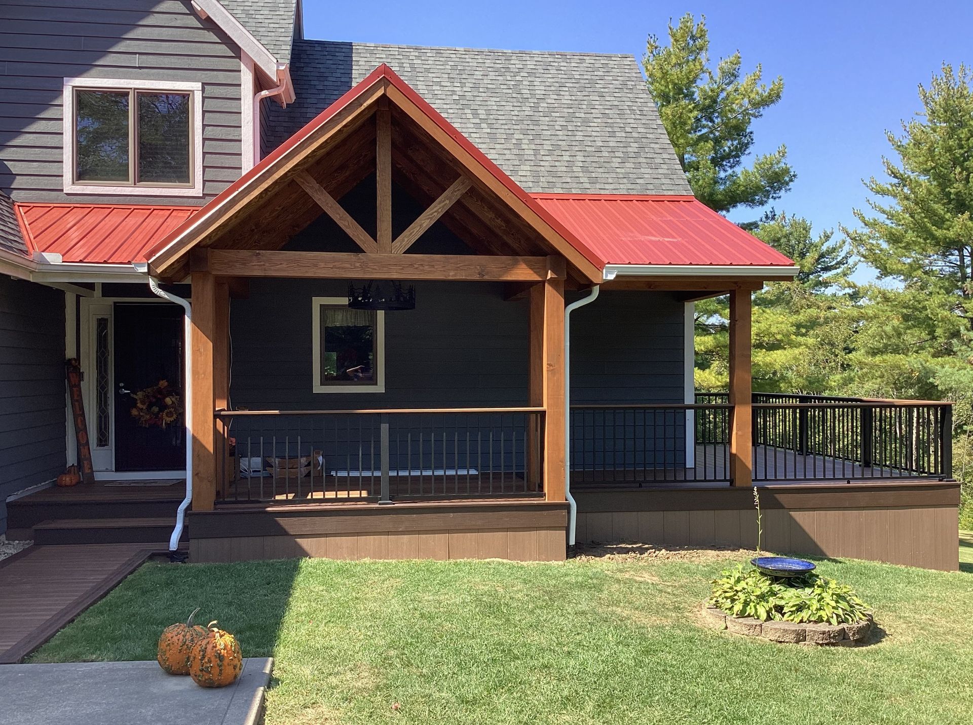 Front porch with dark blue siding, red roof accents, and wooden railings on a sunny day