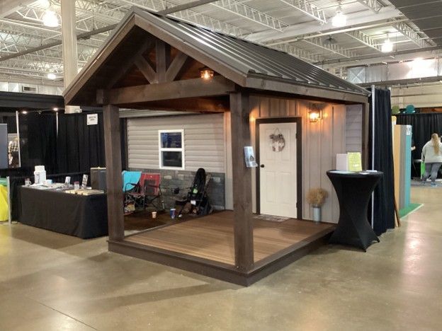 Small wooden cabin-style booth with porch at an indoor trade show, lit by warm lights