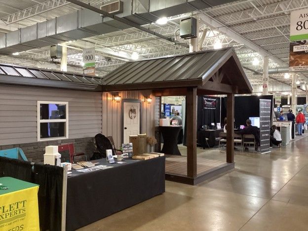 Booth display with a small gray house model and black table at an indoor trade show.