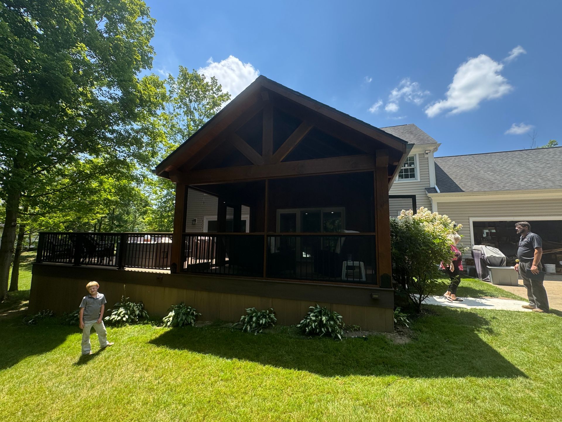 Backyard deck with a wooden pavilion, green lawn, and two people standing outside on a sunny day