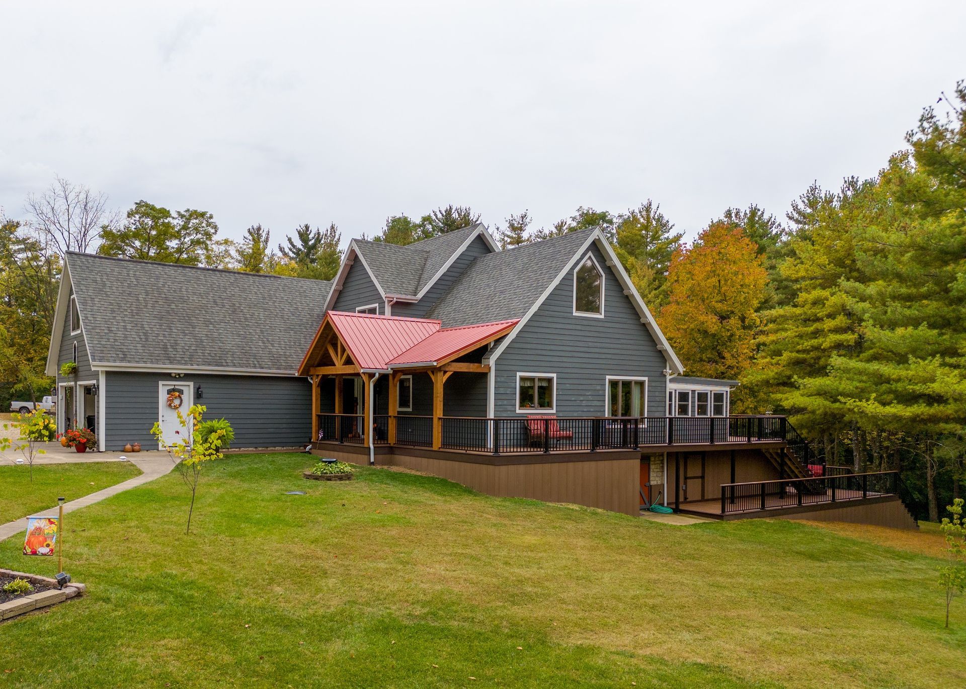 Gray house with red porch on a large grassy lot surrounded by autumn trees