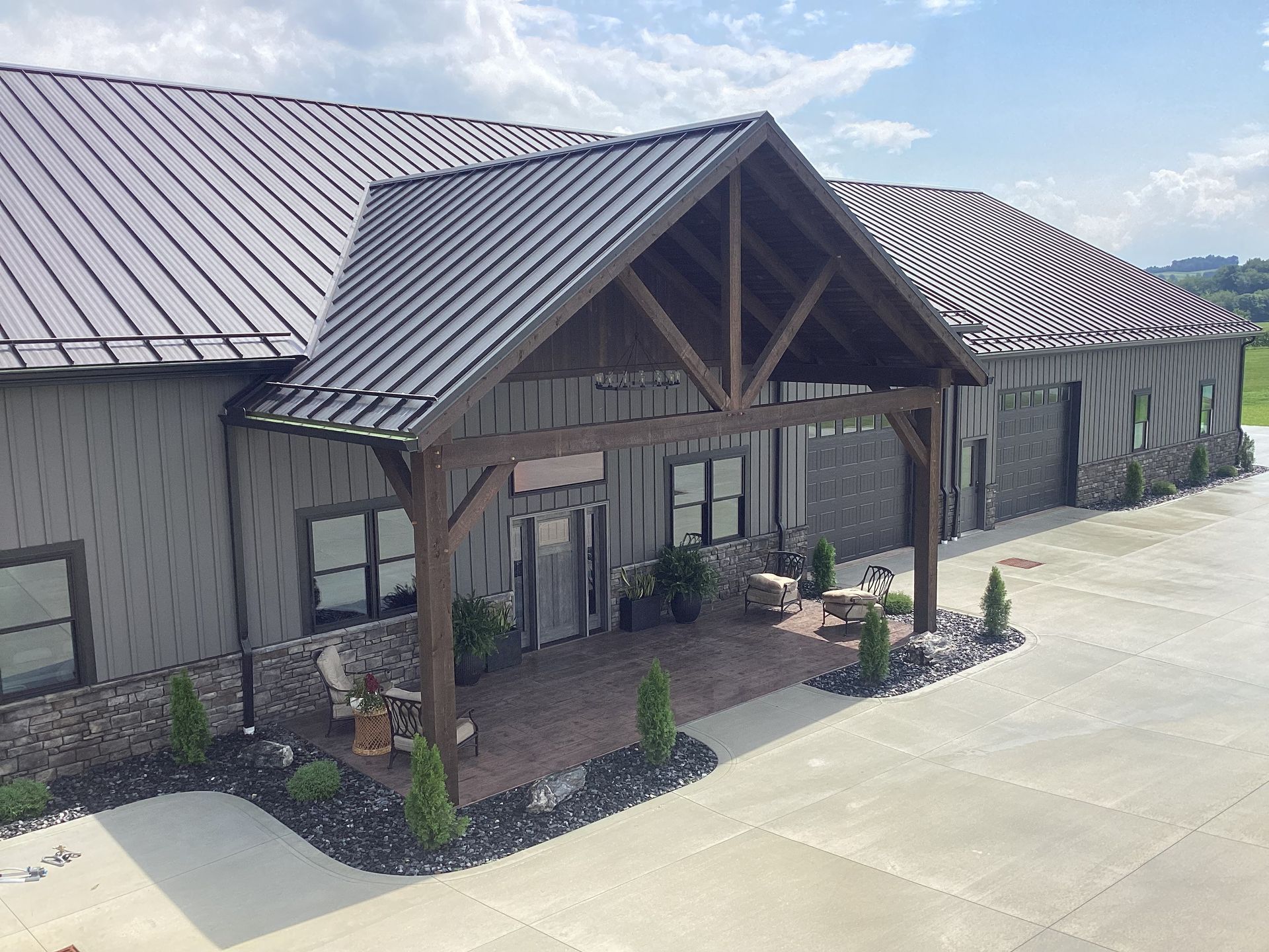 Covered entrance to a gray metal building with a gabled porch and concrete driveway