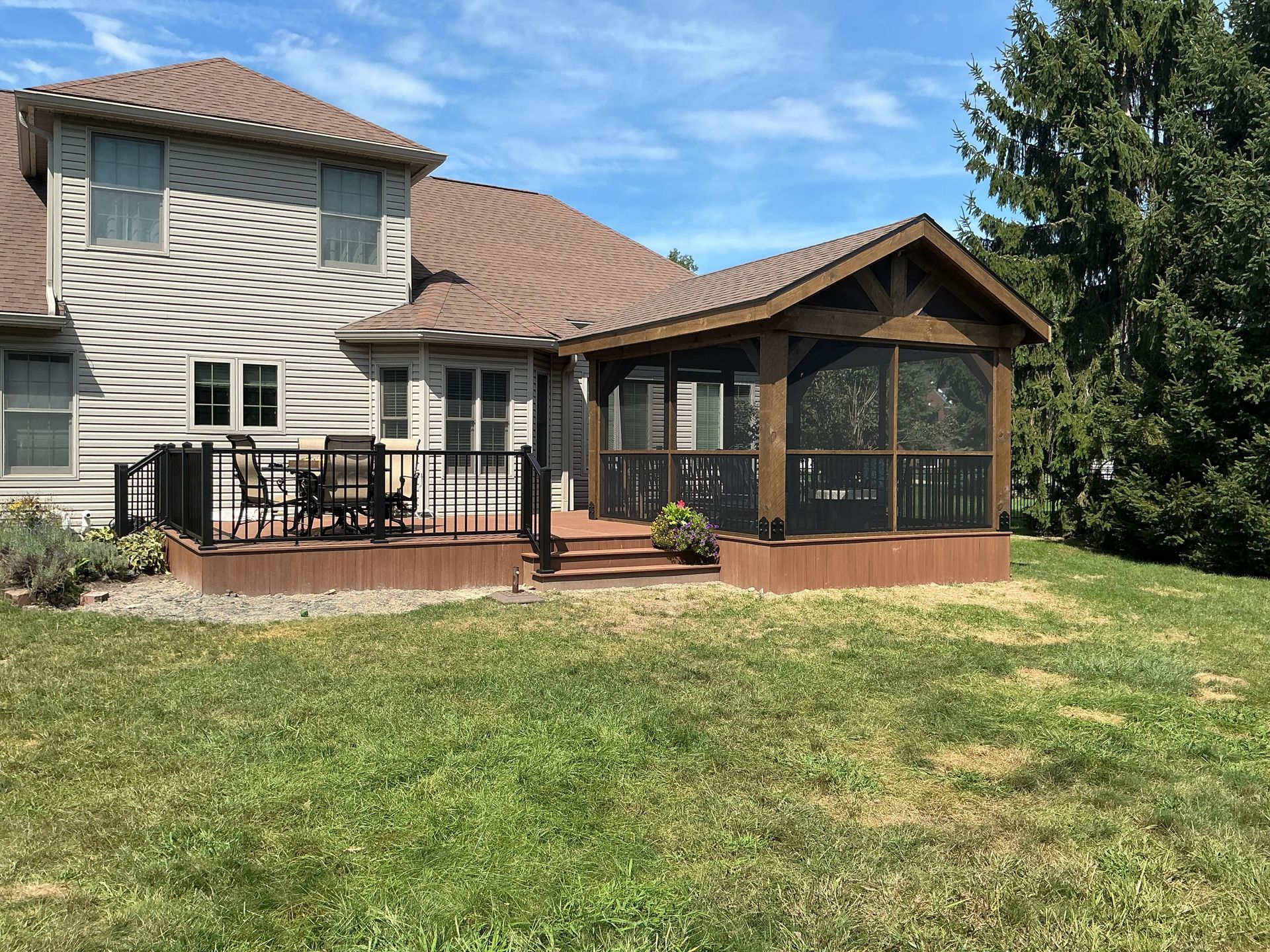Two-story house with screened porch and wooden deck in a grassy backyard