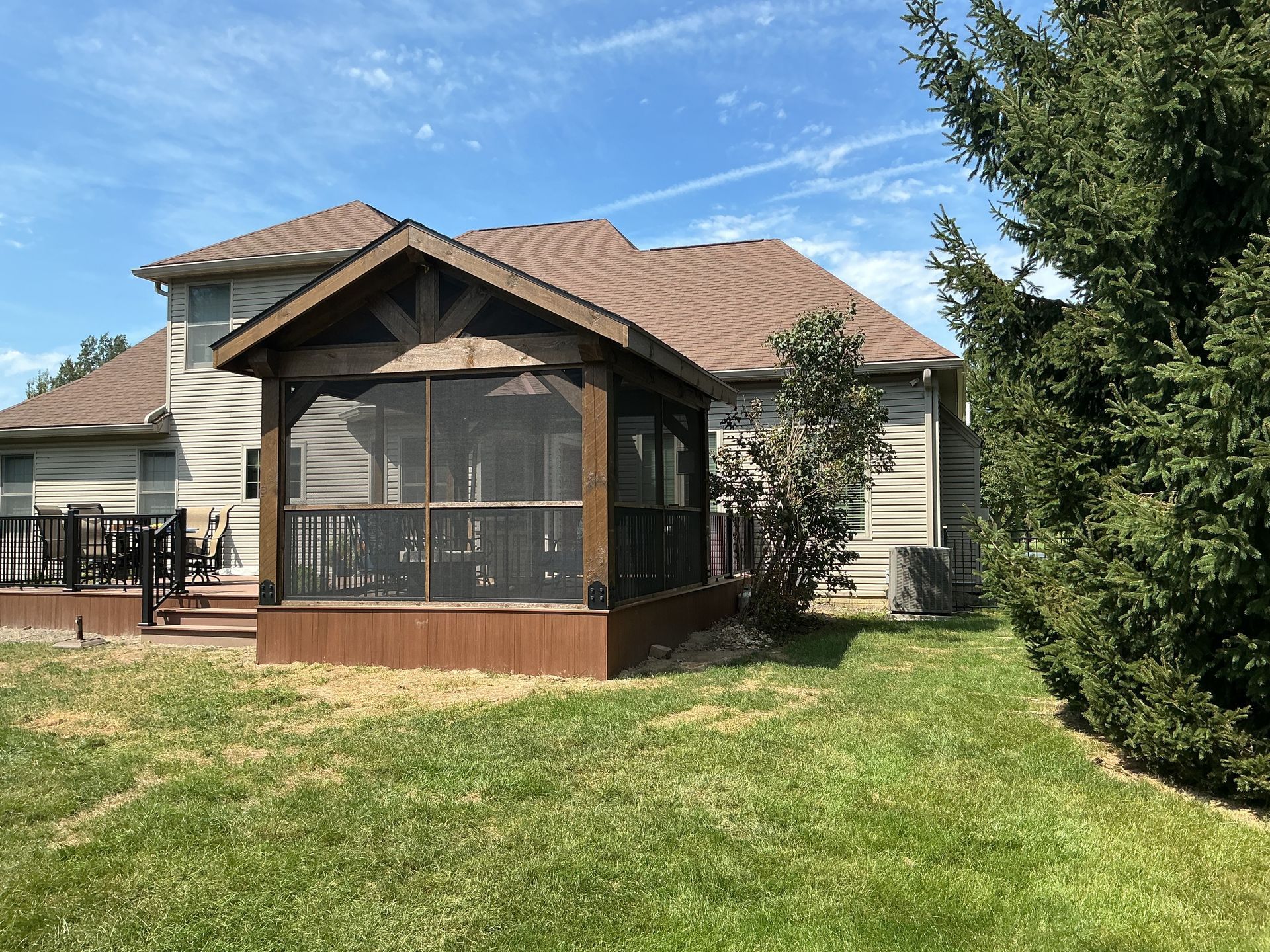 Suburban house with screened porch, brown roof, and green lawn under a blue sky