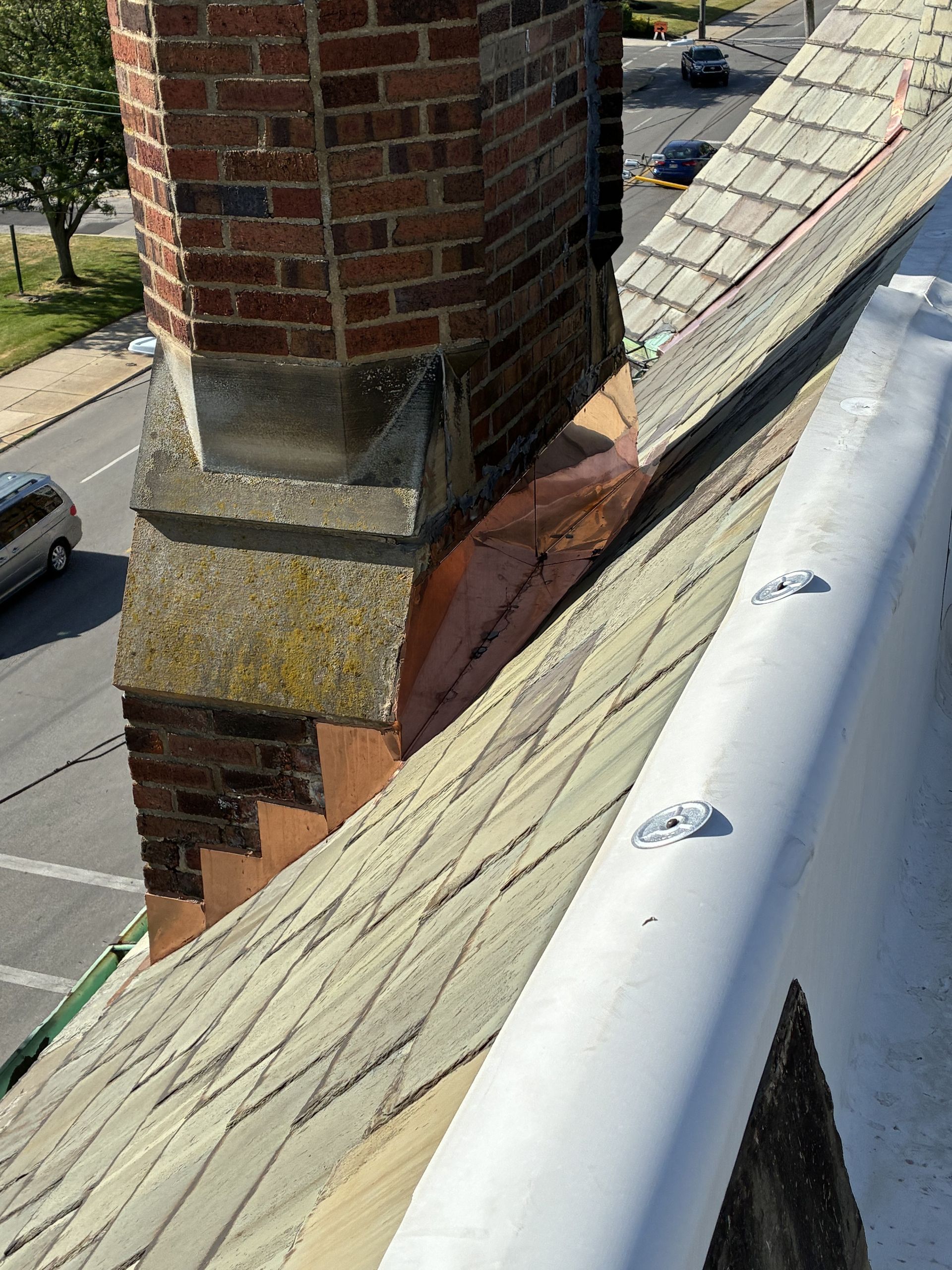 Roof edge with white gutter beside a brick chimney and patched shingles