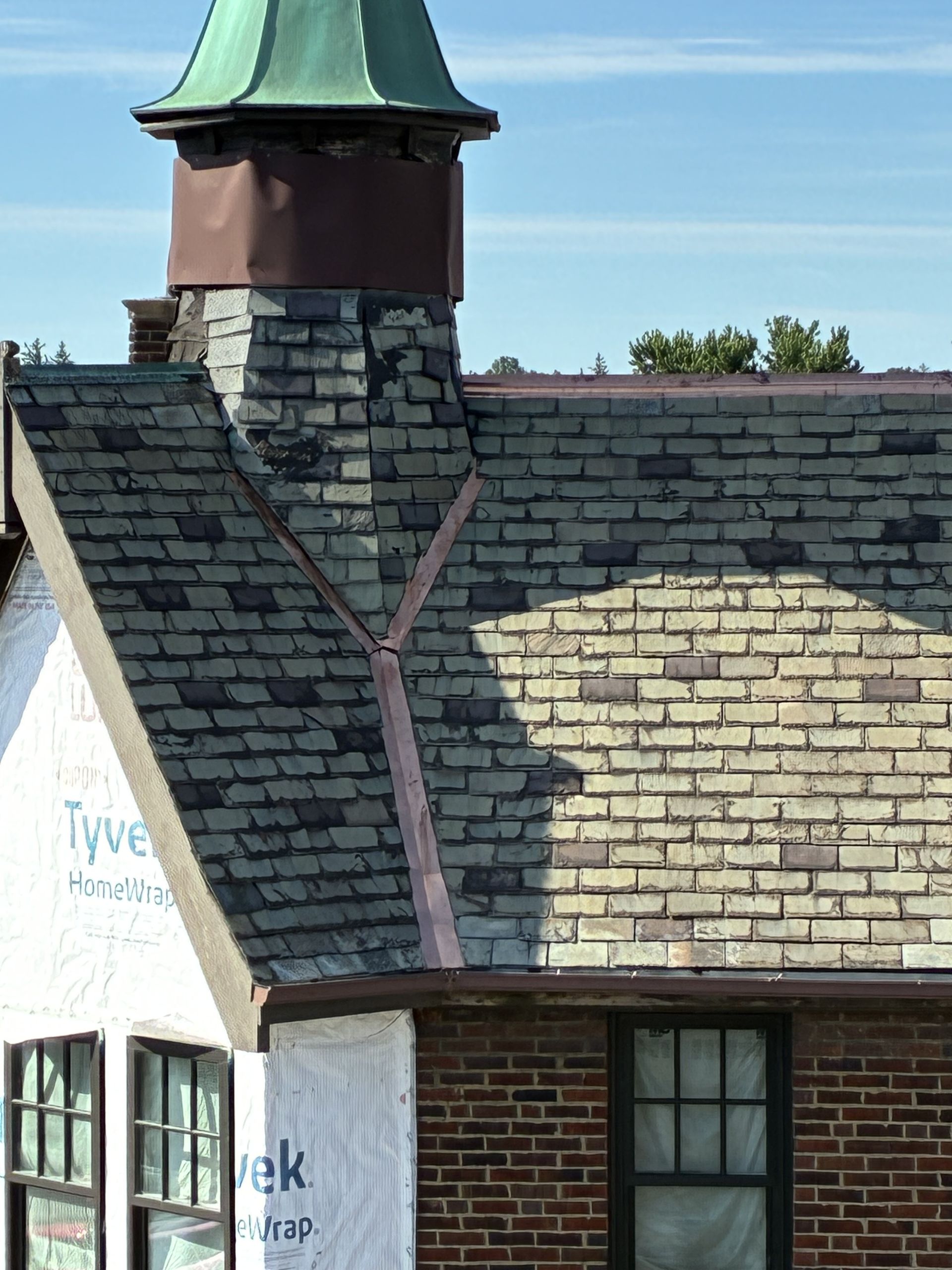 Old brick building with a slate roof and green cupola against a blue sky