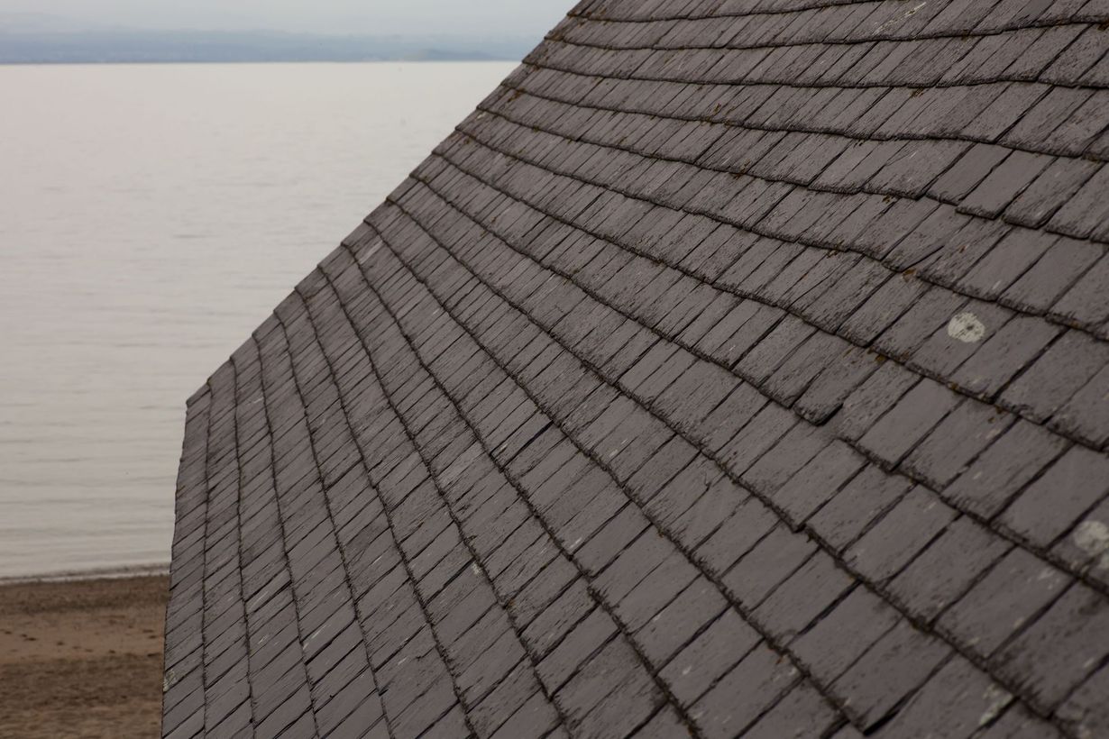Slate roof sloping toward a calm sea under a gray sky