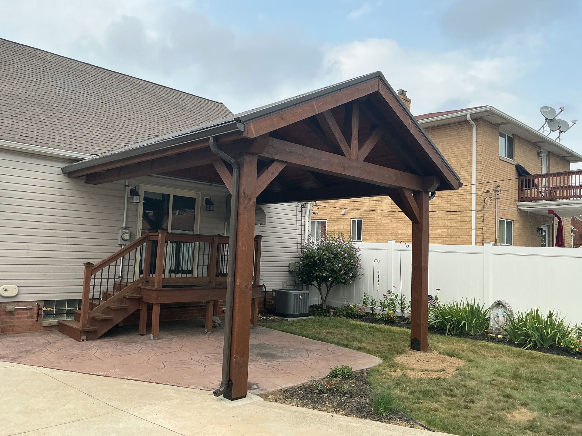 Backyard wooden covered porch with steps beside a house and white fence