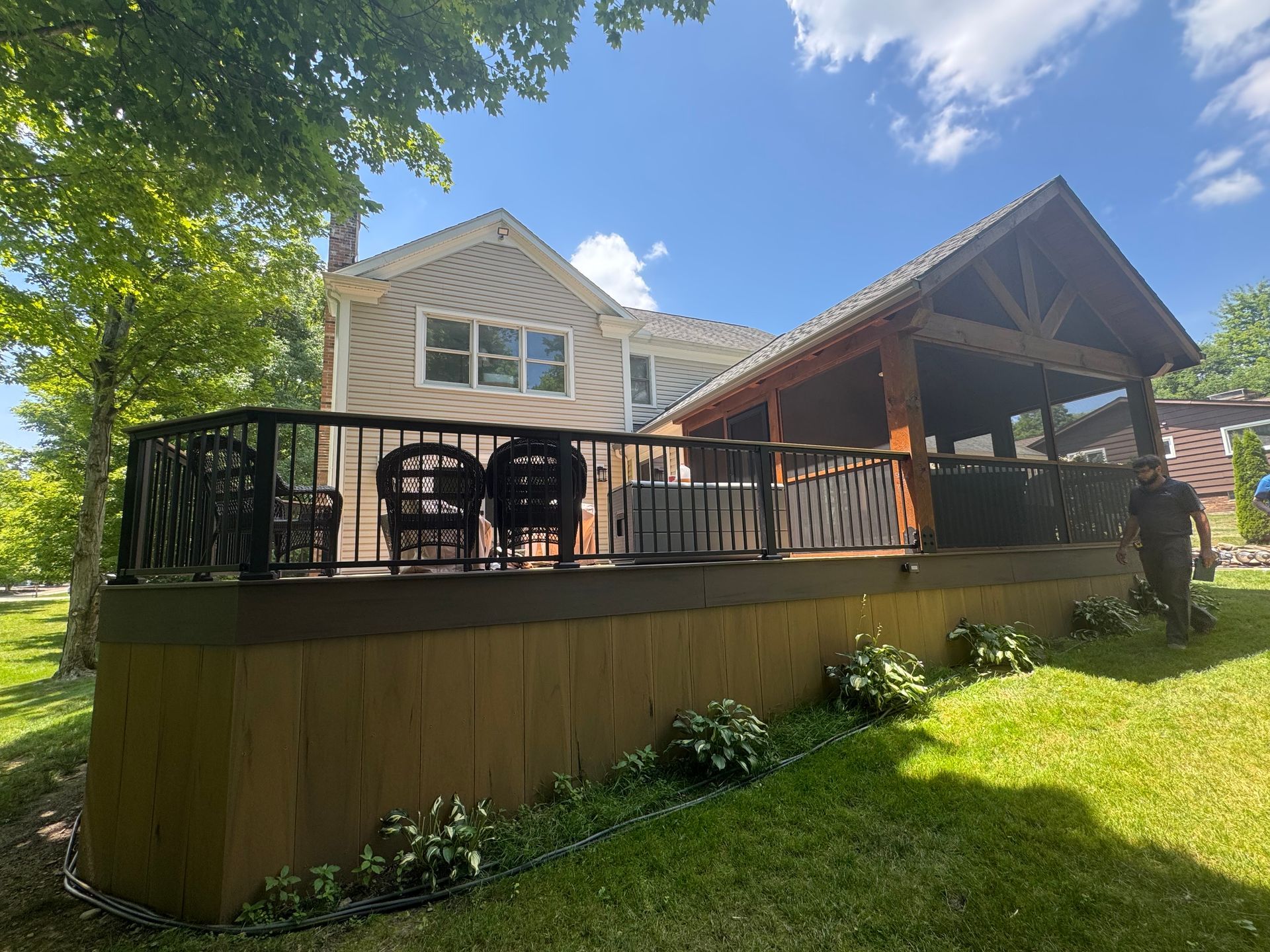Wooden deck with covered patio attached to a house, overlooking a green lawn on a sunny day