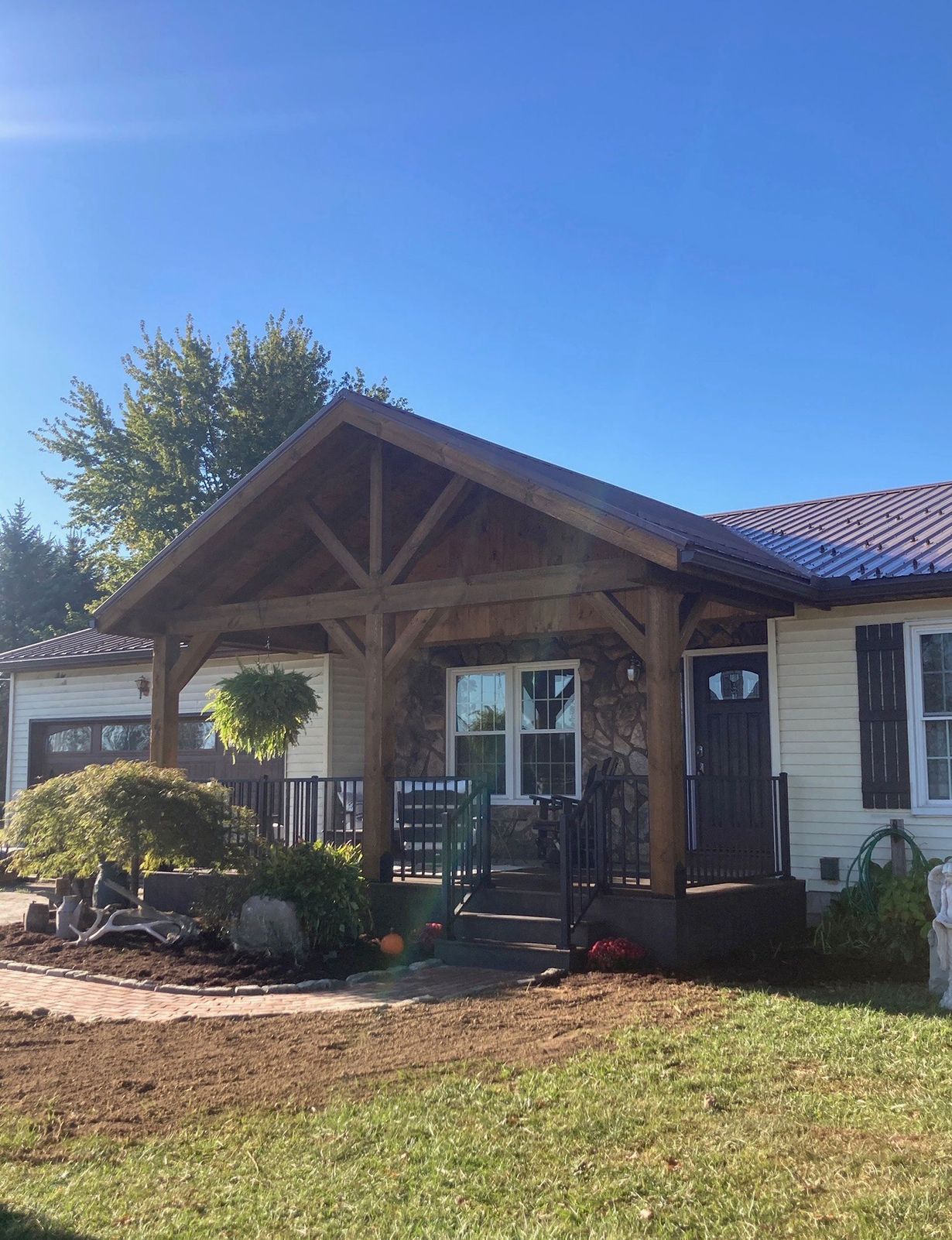 Front porch of a house with a wooden gable roof, white shutters, and a neatly kept lawn under a blue sky