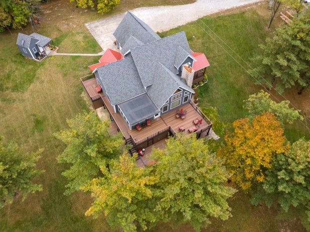 Aerial view of a gray-roofed house with a wooden deck, surrounded by green and autumn trees.