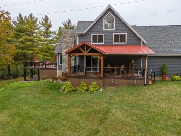 Gray house with a red roof and covered porch, set in a grassy yard with trees and a fenced deck.